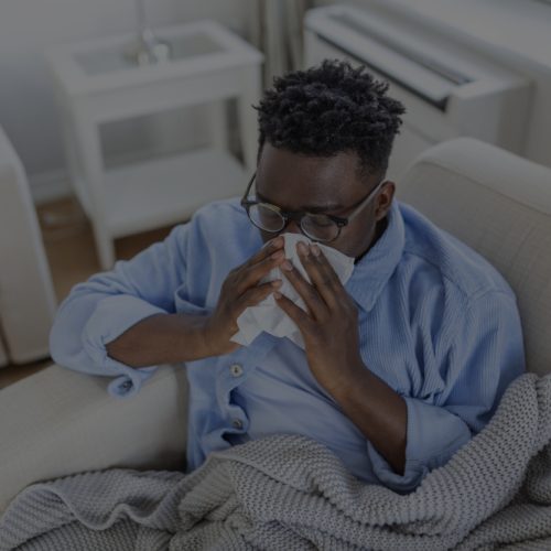Portrait of a sick man with the flu, allergy, germs,cold coughing. Sick Man with headache sitting under the blanket with high fever and a flu, resting and drinking hot beverage Our Definitive Guide to Cold and Flu